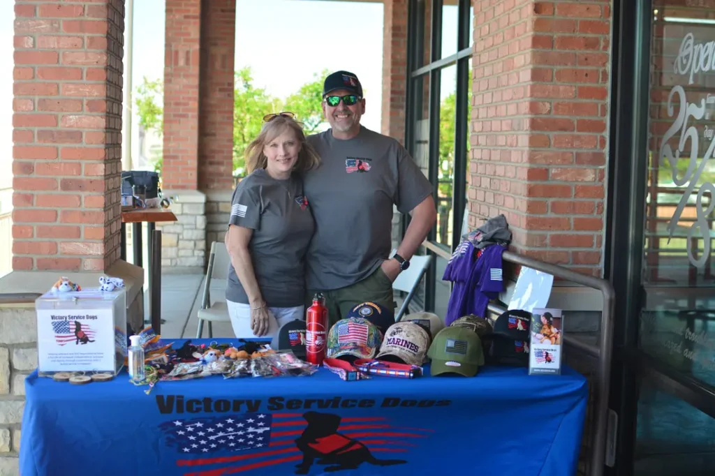 OUR STORY 2 people standing at a Victory Service Dogs Table